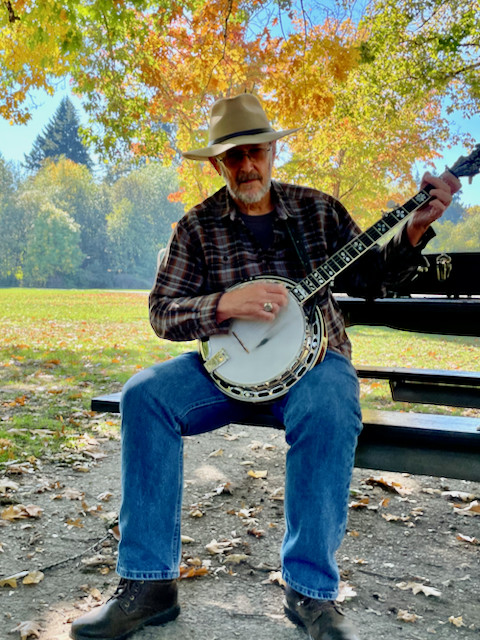 Theron playing banjo in a park with fall leaf colors